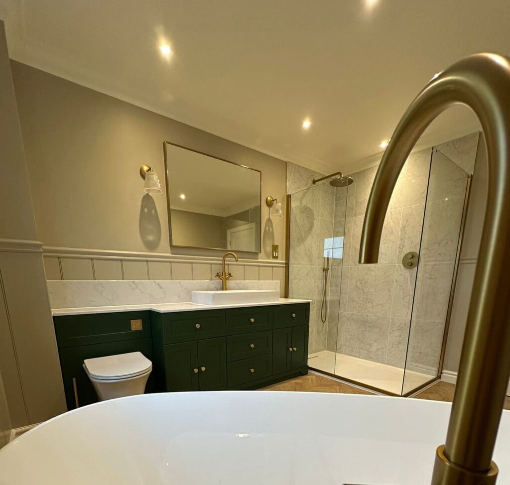 A modern luxury bathroom featuring a large white bathtub, a green vanity with dual sinks, gold fixtures, a large mirror, and a glass shower enclosure with a rainfall showerhead. The walls are light with subtle paneling, and the warm lighting completes this exquisite bathroom design.